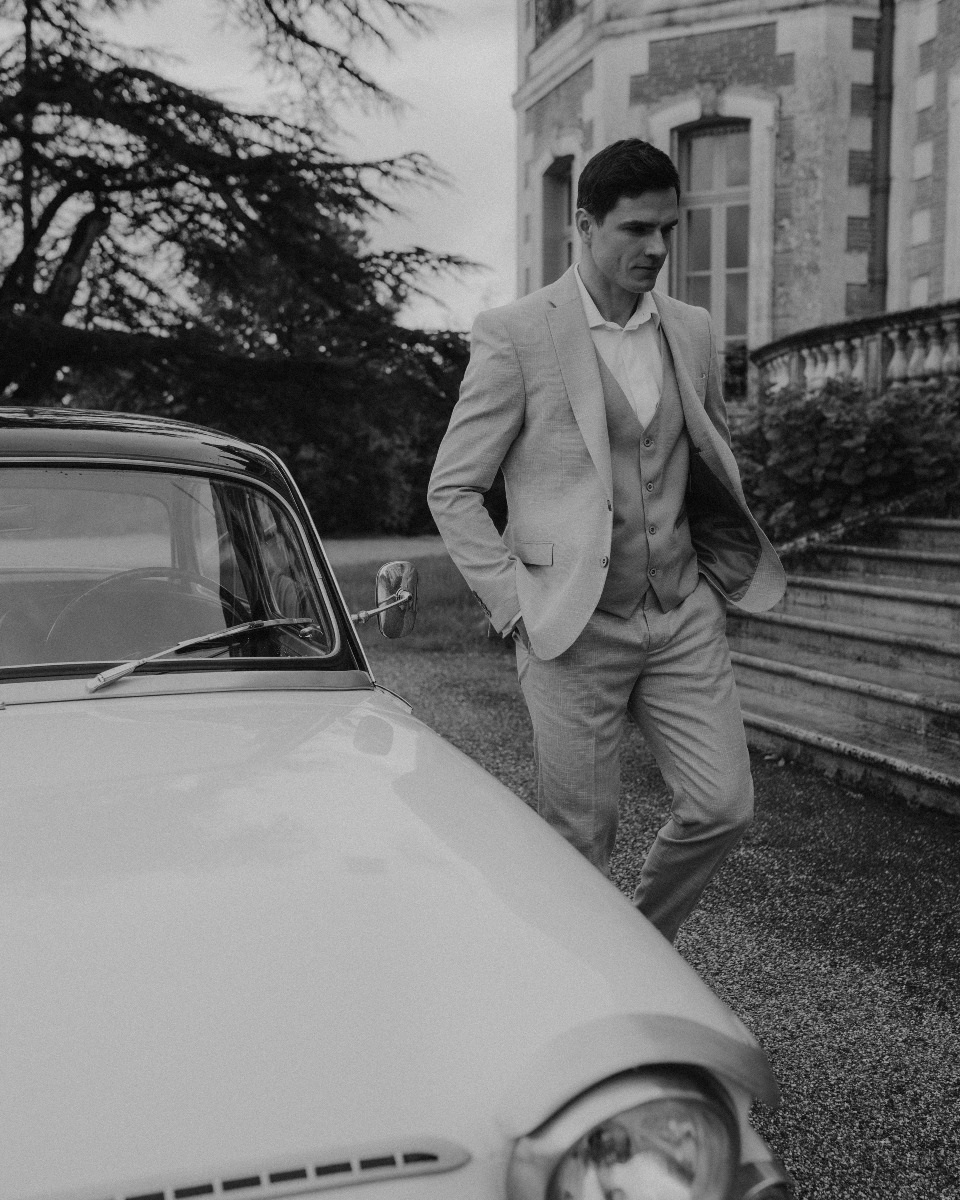 jeune marié dans un costume haut de gamme de location près d'un voiture de collection le jour de son mariage