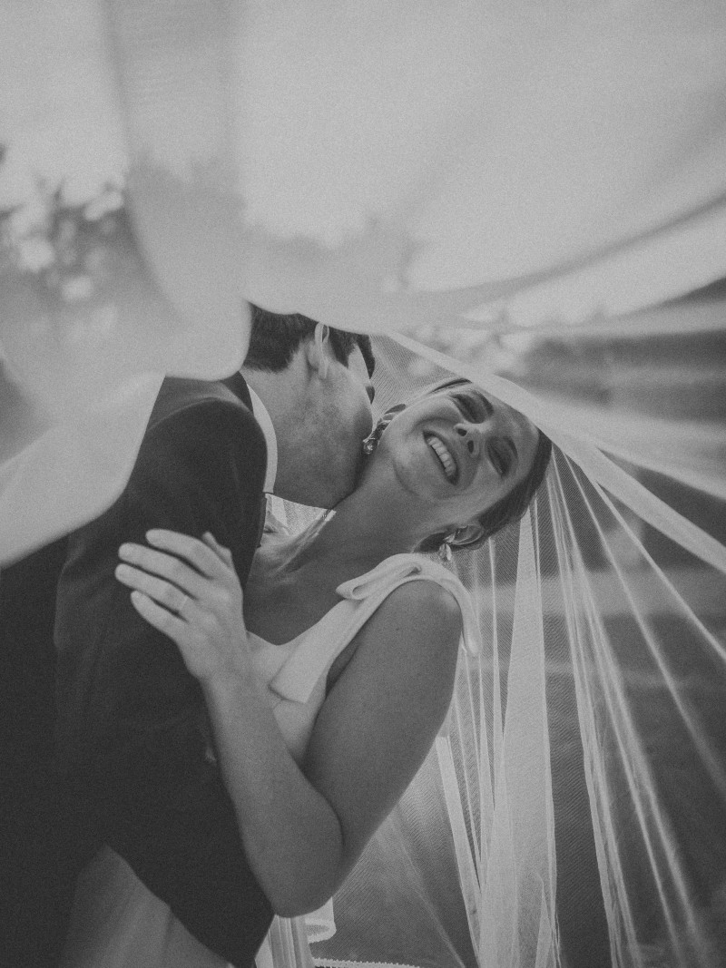 couple de mariés souriant et l'embrassant sous le voile de la mariée